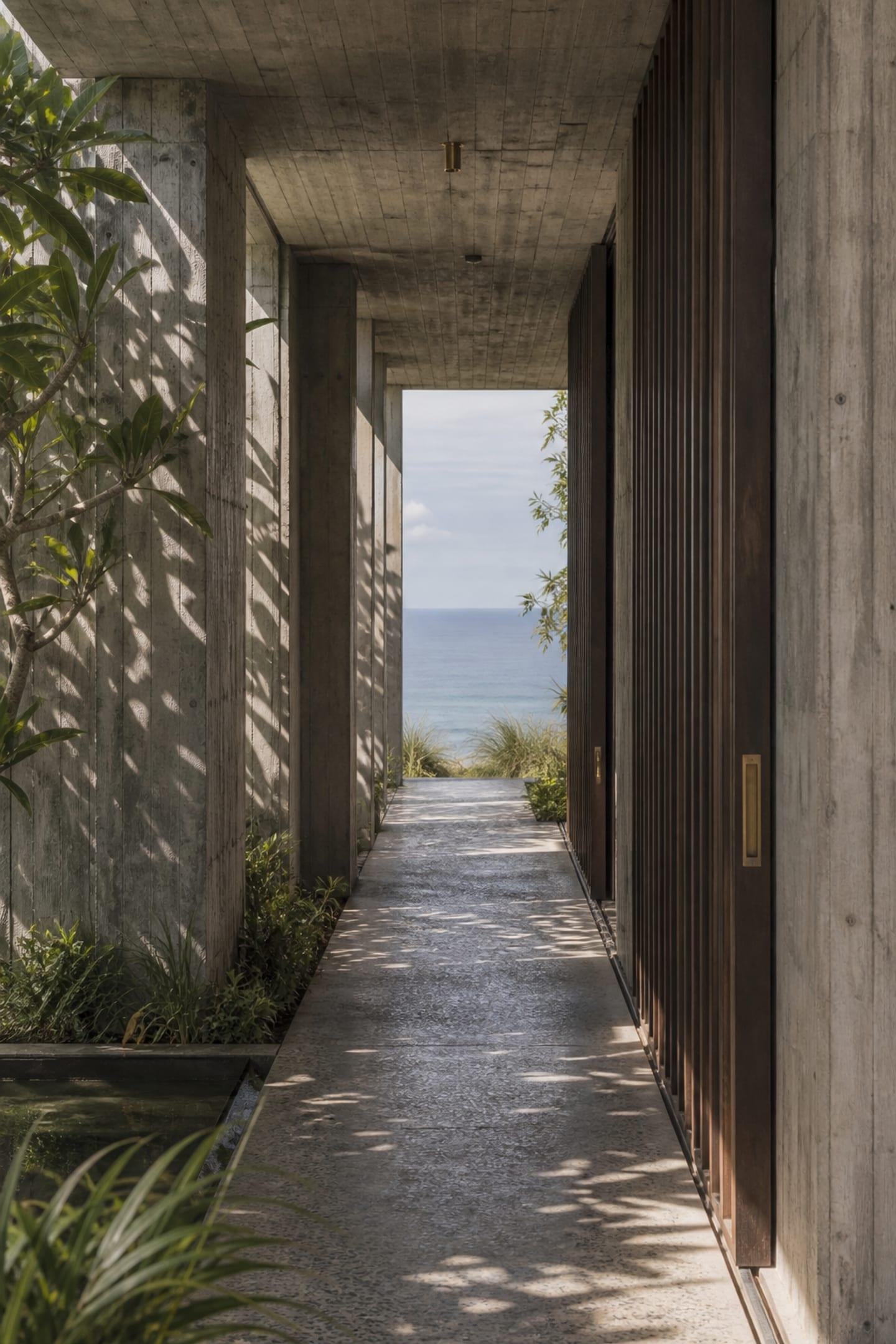 Narrow concrete breezeway with dappled light and a framed sea horizon