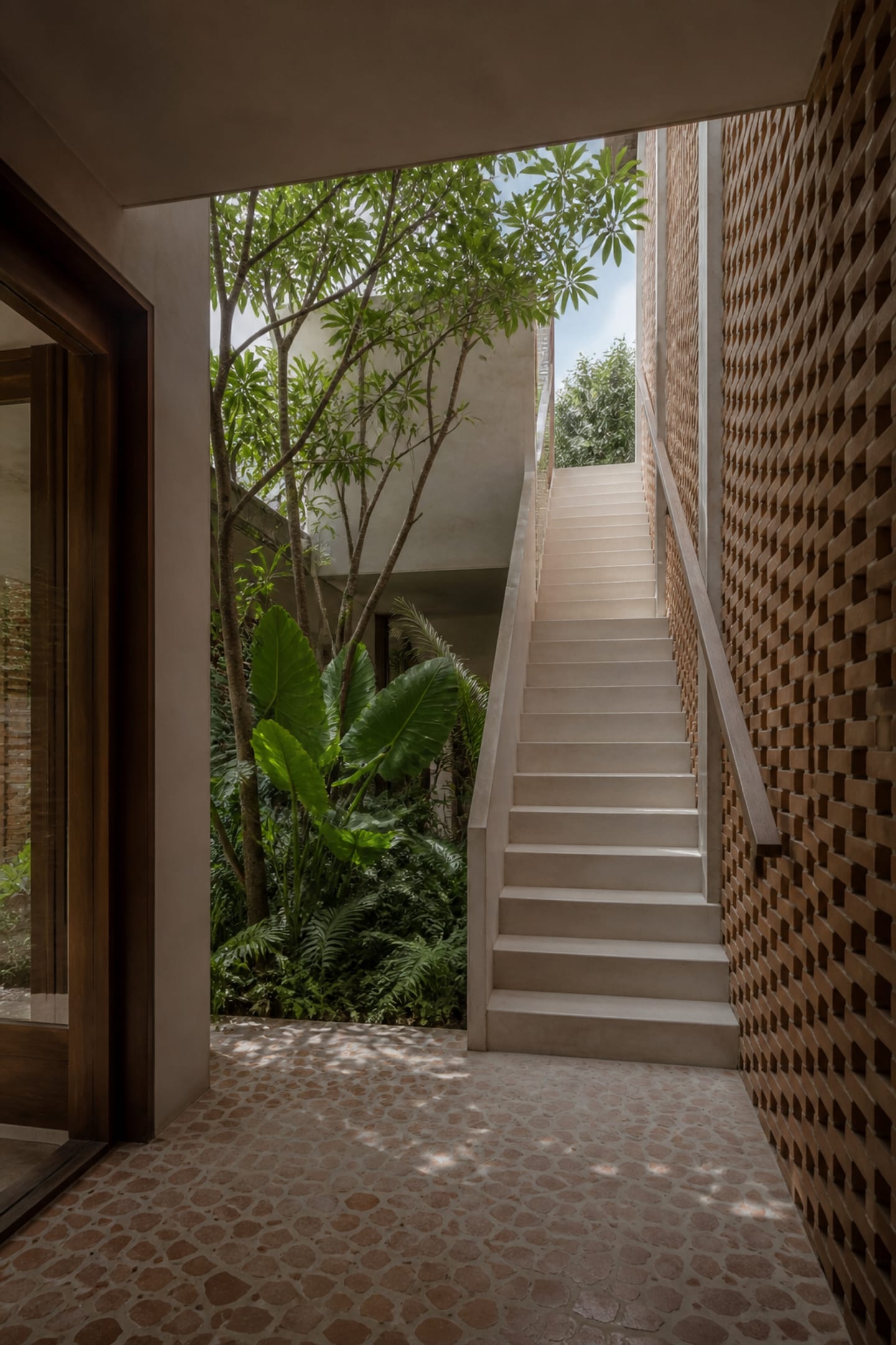 Sculptural stair rising beside tall courtyard planting and perforated brick