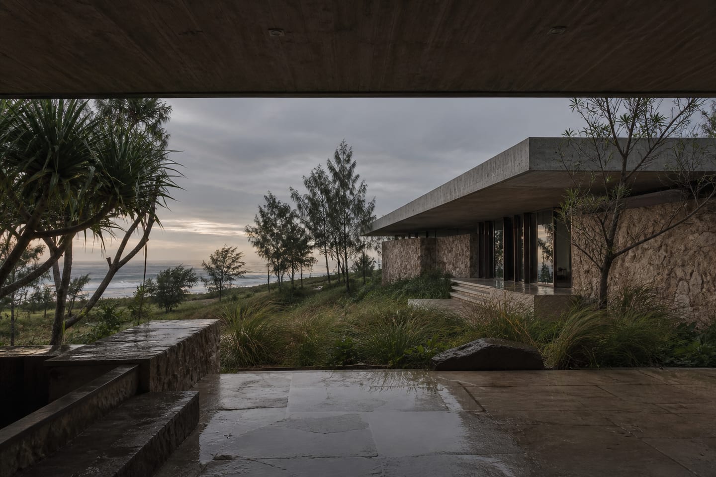 Quiet concrete pavilion opening through coastal grasses toward a hazy sea